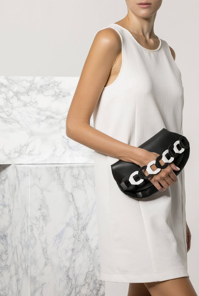 Black leather clutch bag with white details on the handwoven chain handle