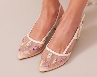 May include: Ivory slingback heels with a pointed toe. The sheer mesh upper is embroidered with white, purple, and gold floral designs. The heels have a small block heel and a delicate ankle strap.