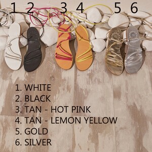 May include: Six pairs of sandals in different colours, labelled with numbers 1 through 6. The colours are white, black, tan with hot pink laces, tan with lemon yellow laces, gold, and silver.