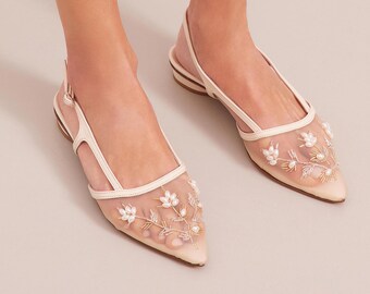 May include: Ivory-colored slingback flats with a pointed toe. The flats feature a sheer mesh overlay adorned with embroidered white flowers and small pearls. The straps and trim are a solid ivory color.
