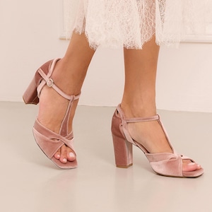 Puede incluir: Sandalias de tacón de terciopelo rosa empolvado. Los zapatos de punta abierta tienen un diseño de tira en T y una correa en el tobillo con hebilla. Los tacones de bloque miden aproximadamente 7,6 cm de alto.