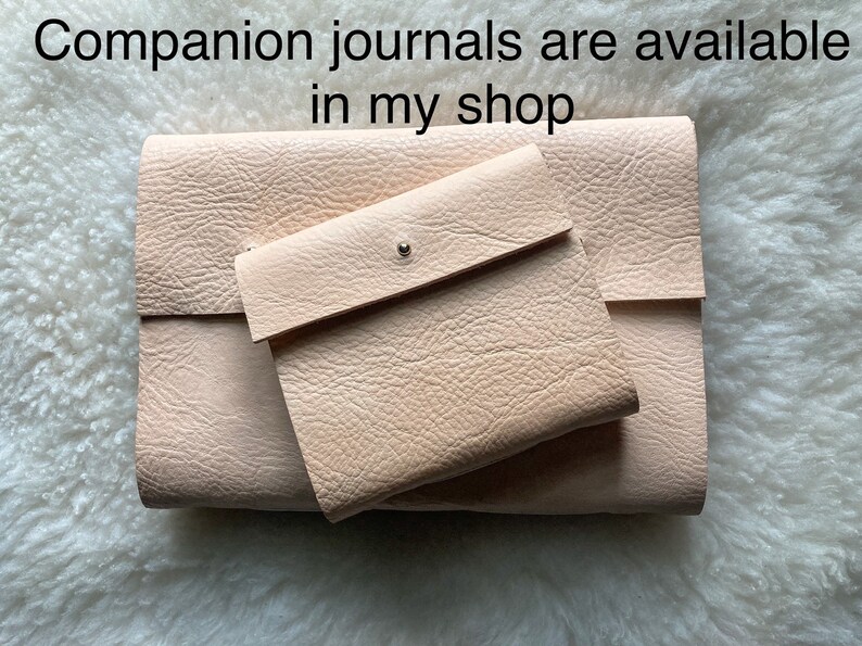 May include: A set of light beige leather journals and a small matching pouch. The journals are rectangular with a textured surface. The pouch has a flap closure with a silver snap. Text at the top says "Companion journals are available in my shop."