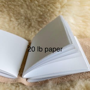 May include: An open notebook with white pages, labelled "20 lb paper." The pages are clean and appear to be of good quality. The notebook is displayed open, revealing the inner pages, against a neutral backdrop.