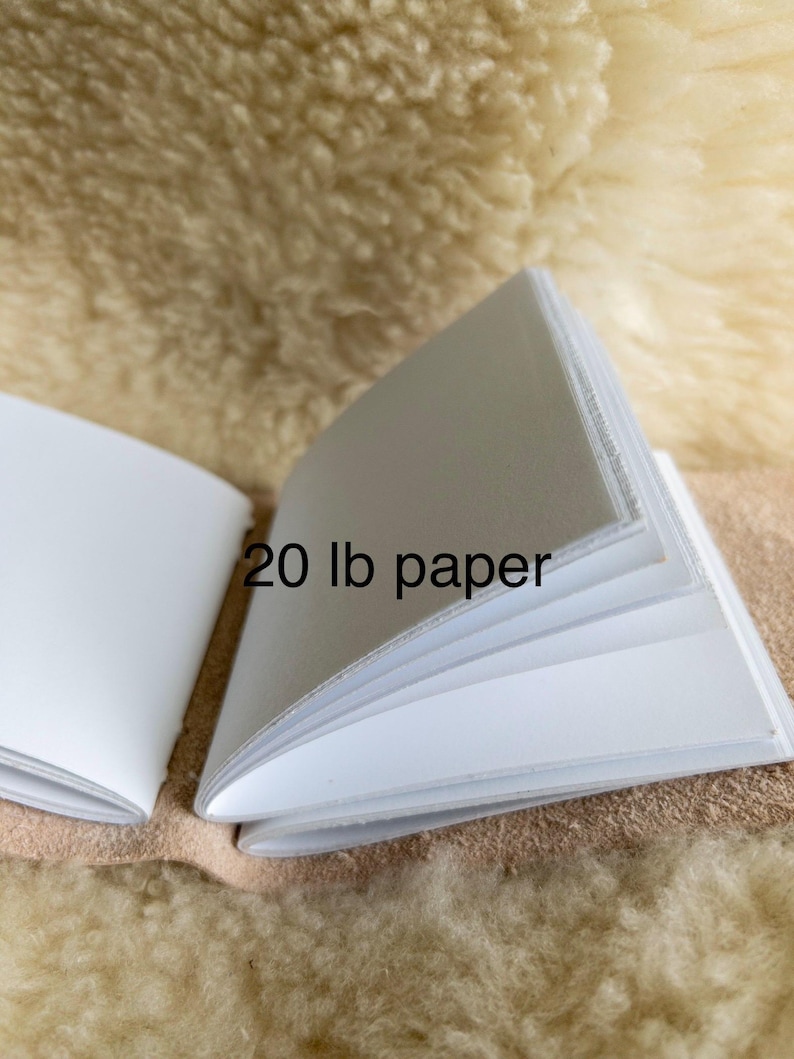 May include: An open notebook with white pages, labelled "20 lb paper." The pages are clean and appear to be of good quality. The notebook is displayed open, revealing the inner pages, against a neutral backdrop.