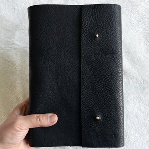 May include: Black leather-bound journal with gold accents. The journal has a textured cover and a flap closure.