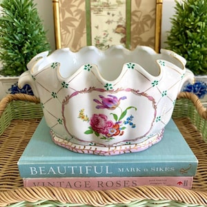 May include: A white ceramic planter with a scalloped rim, gold trim, and floral designs. The planter sits atop two books on a wicker tray. The books are titled "BEAUTIFUL" and "VINTAGE ROSES".
