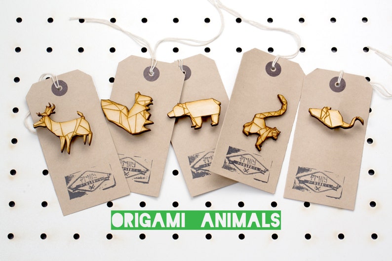 May include: Five wooden origami animal pins on brown paper tags with the text "Origami Animals". The animals are a deer, a fox, a bear, a monkey, and a bat.
