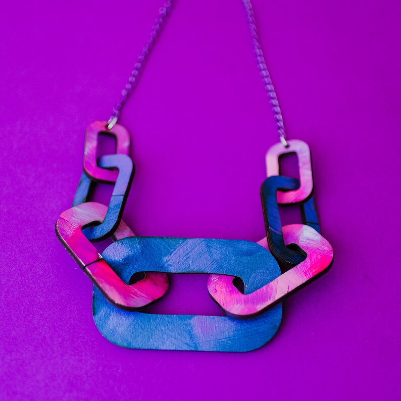 Op de afbeelding: Een kleurrijke houten ketting met grote, dikke schakels in tinten blauw en roze. De ketting is gemaakt van geschilderd hout en heeft een zilveren ketting.