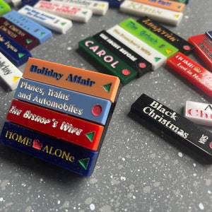 Peut inclure: Une pile de cinq blocs rectangulaires colorés avec des titres de films imprimés dessus. Les titres sont "Holiday Affair", "Planes, Trains and Automobiles", "The Bishop's Wife", "Home Alone", et "Black Christmas".