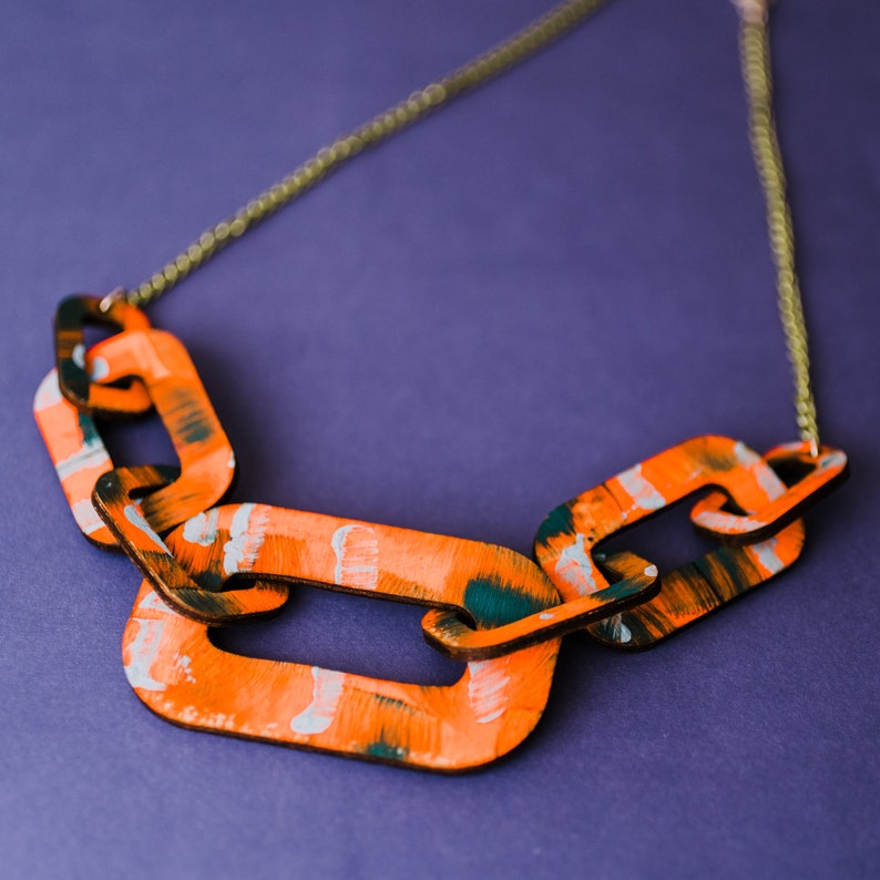 Op de afbeelding: Een ketting gemaakt van oranje en groene geverfde houten schakels. De schakels zijn verbonden door een gouden ketting.
