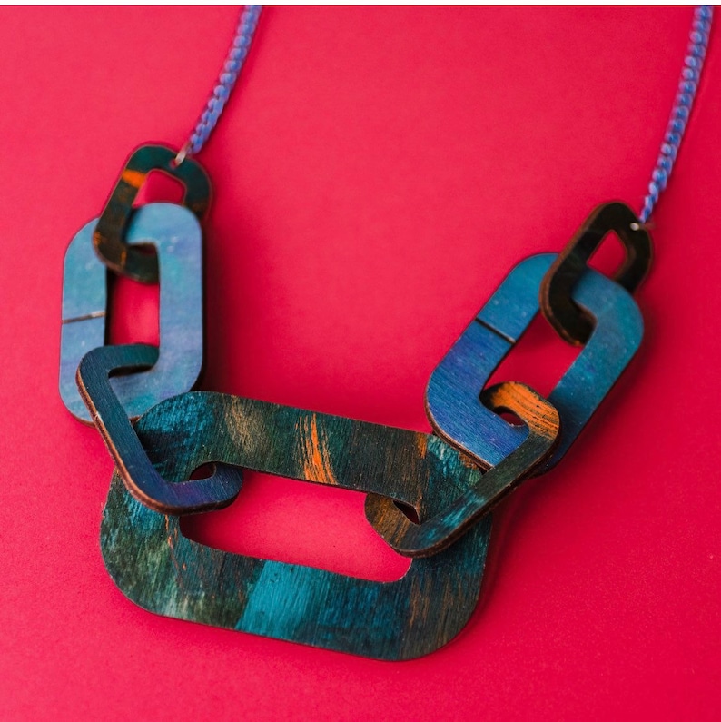 Op de afbeelding: Een blauwe en groene houten ketting met een kettingschakelontwerp. De schakels zijn groot en hebben een getextureerd oppervlak.