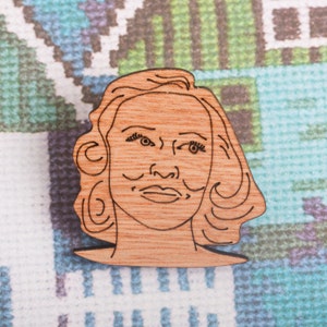 May include: A wooden cutout of a woman's face with a simple line drawing of her hair and features.