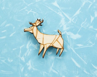 May include: A wooden deer figurine with a geometric design. The deer is light brown with darker brown outlines, set against a light blue background. The antlers and legs are clearly defined.