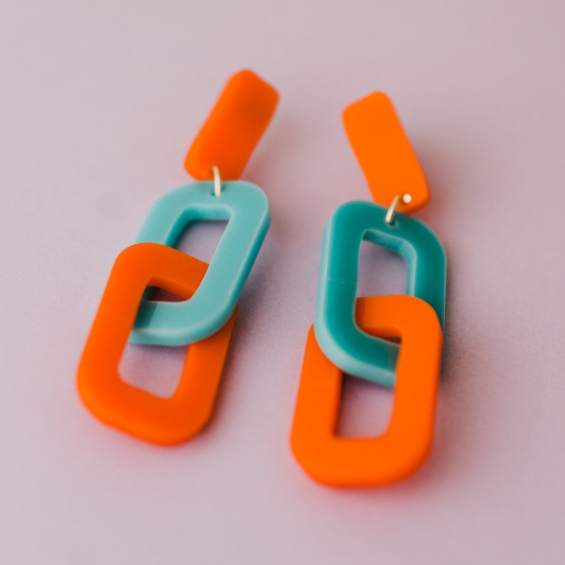 May include: A pair of orange and teal statement earrings with a linked chain design.