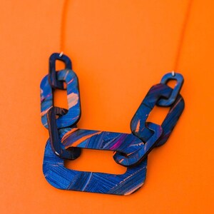 Op de afbeelding: Een blauwe en paarse geschilderde houten ketting met een kettingschakelontwerp. De ketting is gemaakt van meerdere schakels die aan elkaar zijn verbonden.