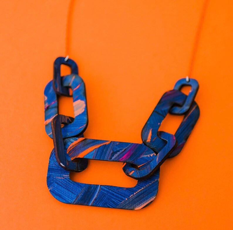 Op de afbeelding: Een blauwe en paarse geschilderde houten ketting met een kettingschakelontwerp. De ketting is gemaakt van meerdere schakels die aan elkaar zijn verbonden.