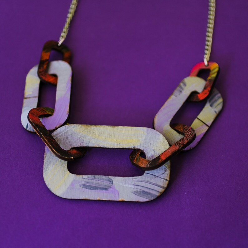 Op de afbeelding: Een kleurrijke houten kettingketting met een zilveren ketting. De schakels zijn geschilderd in tinten paars, geel, rood en oranje.