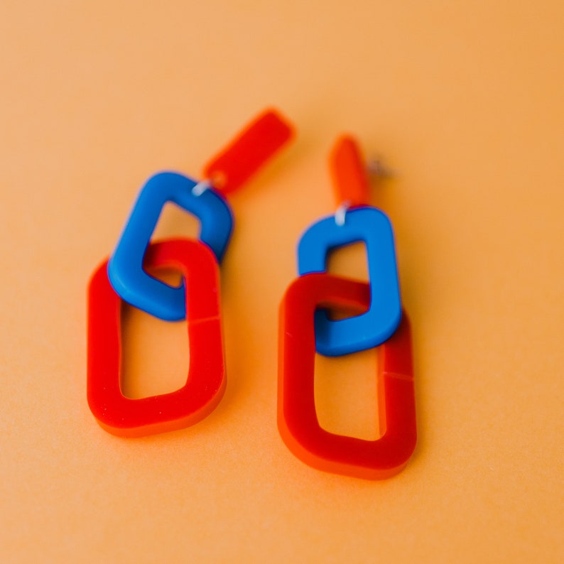 May include: A pair of red and blue acrylic earrings with a linked chain design.