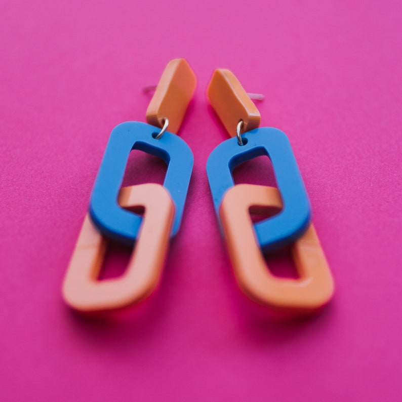 May include: A pair of orange and blue acrylic earrings with a linked chain design.