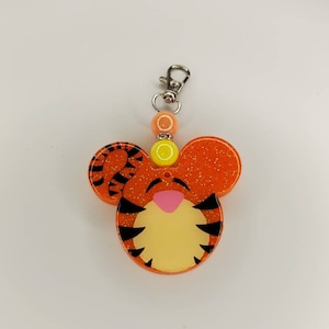 May include: Orange and black glitter Tigger keychain with a pink nose and yellow eyes. The keychain has a silver metal clasp.