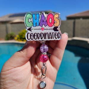 May include: A rainbow glitter badge holder with the text "Chaos Coordinator" and a pink heart. The holder has a clear plastic badge clip and a beaded chain with pink and purple beads.