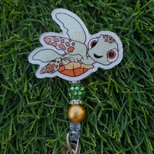 May include: A sparkly silver turtle with orange spots and green and gold beads attached to a clear retractable badge holder.