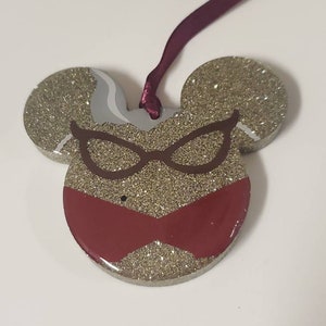 Peut inclure: Ornement en forme de souris en paillettes dor&eacute;es avec un motif rouge et marron de lunettes et d'un n&oelig;ud.