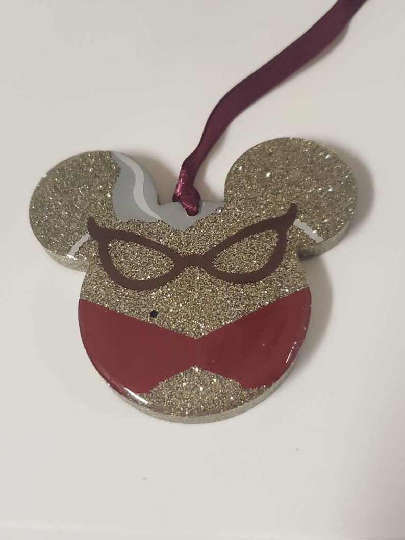 Peut inclure: Ornement en forme de souris en paillettes dor&eacute;es avec un motif rouge et marron de lunettes et d'un n&oelig;ud.