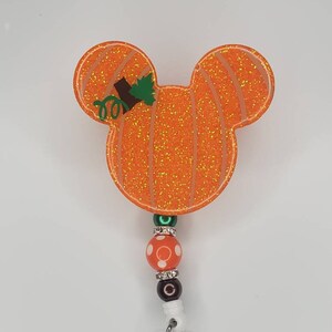 May include: Orange glitter pumpkin shaped badge holder with a green stem and white polka dot beads.