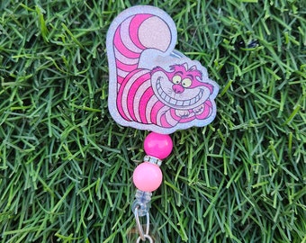 Op de afbeelding: Roze en witte glitter Cheshire Cat badge reel met roze kralen.