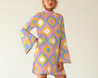 May include: A colorful, patterned mini dress with long bell sleeves. The dress features a high neckline and a retro design in pink, yellow, blue, and white. The outfit is completed with white knee-high boots.