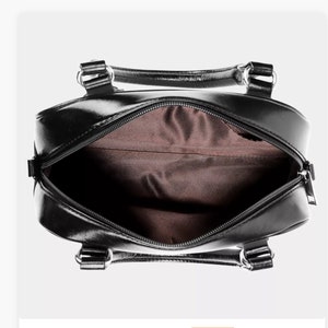 May include: Black leather handbag with a zipper closure and two top handles. The bag is open and the inside is lined with brown fabric.