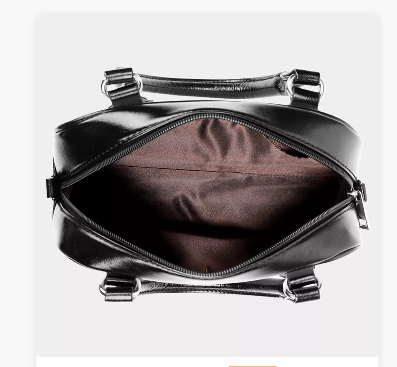 May include: Black leather handbag with a zipper closure and two top handles. The bag is open and the inside is lined with brown fabric.
