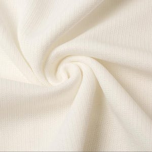 May include: Close-up of a cream-colored fabric with a textured weave. The fabric is draped and folded, creating soft shadows and highlights. The material appears to be lightweight and breathable, suitable for clothing or home decor.