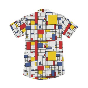 Puede incluir: Una camisa blanca de manga corta con botones y un patr&oacute;n geom&eacute;trico en cuadrados rojos, amarillos y azules.