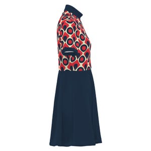 May include: A short-sleeved dress featuring a navy blue skirt and a patterned bodice. The bodice has a cream background with red circles and black accents. The dress has a high, navy blue collar and short sleeves with navy blue trim.