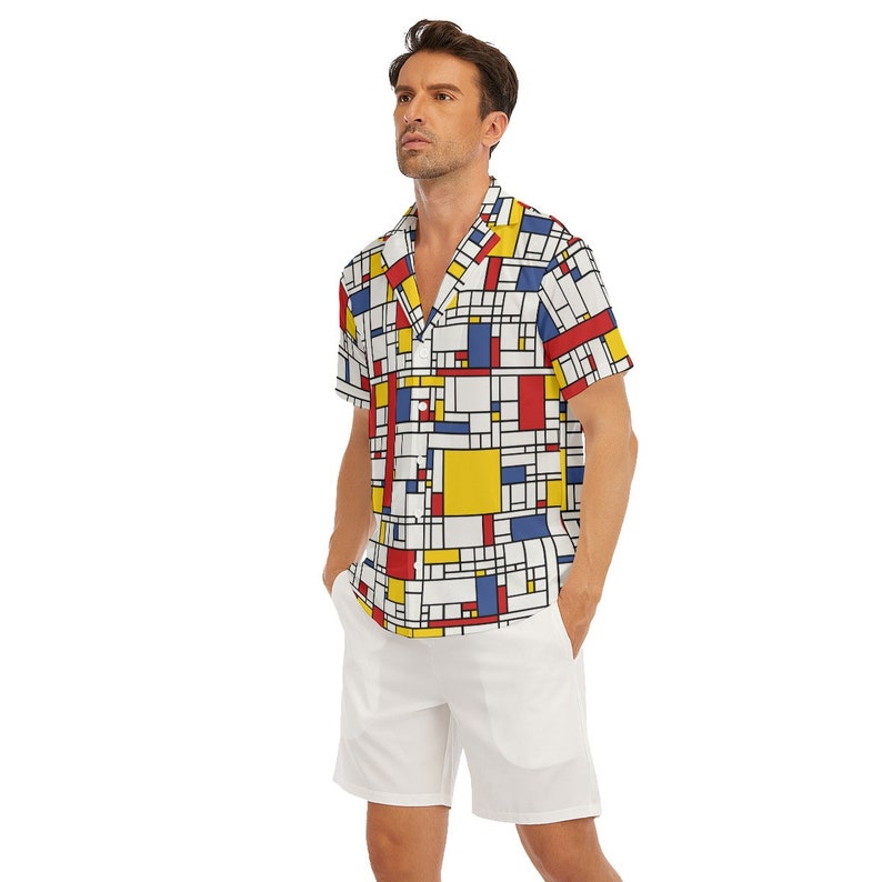 Puede incluir: Una camisa blanca de manga corta con botones y un patr&oacute;n geom&eacute;trico en rojo, azul y amarillo. La camisa tiene cuello y un ajuste holgado.