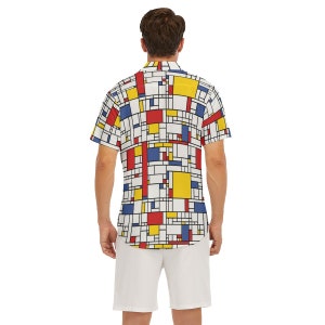 Puede incluir: Una camisa blanca de manga corta con botones y un patr&oacute;n geom&eacute;trico en rojo, amarillo y azul. La camisa tiene cuello y cierre de botones.