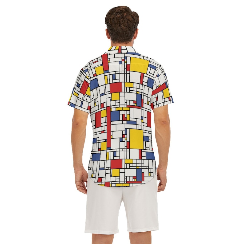 Puede incluir: Una camisa blanca de manga corta con botones y un patr&oacute;n geom&eacute;trico en rojo, amarillo y azul. La camisa tiene cuello y cierre de botones.