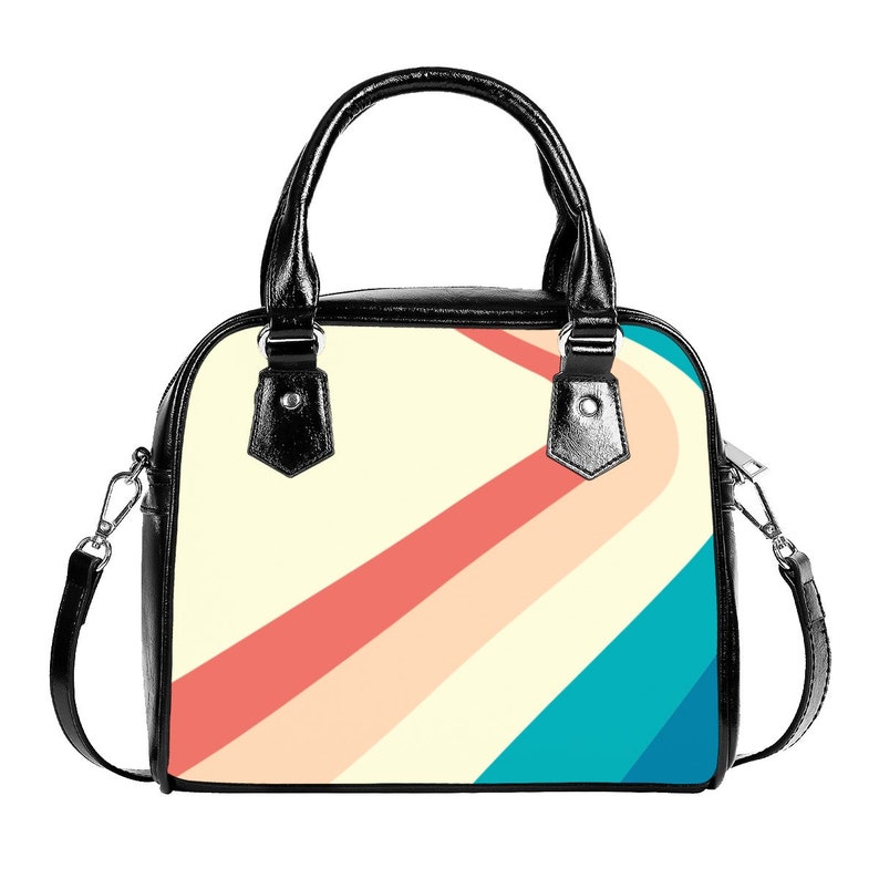 K&ouml;nnte beinhalten: Eine schwarze Ledertasche mit einem farbenfrohen geometrischen Muster auf der Vorderseite. Das Muster zeigt diagonale Streifen in den Farben Pfirsich, Creme und T&uuml;rkis.
