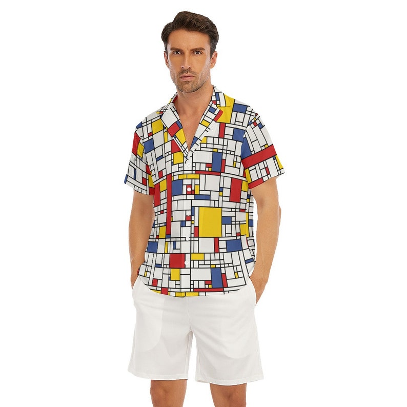 Puede incluir: Una camisa blanca de manga corta con botones y un patr&oacute;n geom&eacute;trico en rojo, amarillo, azul y negro. La camisa tiene cuello y un bolsillo en el lado izquierdo. El modelo lleva pantalones cortos blancos.