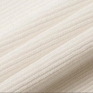 May include: Close-up of a textured, off-white fabric with a ribbed pattern. The fabric is draped, creating soft folds and shadows. The texture appears to be a knit or woven material, possibly used for clothing or home decor.