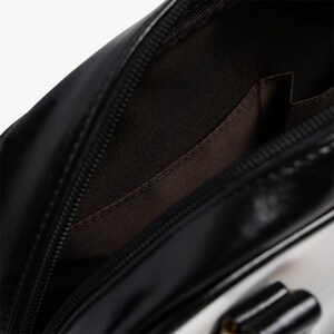 May include: Black and white leather handbag with a zipper closure and a small interior pocket. The bag has a smooth, shiny finish.