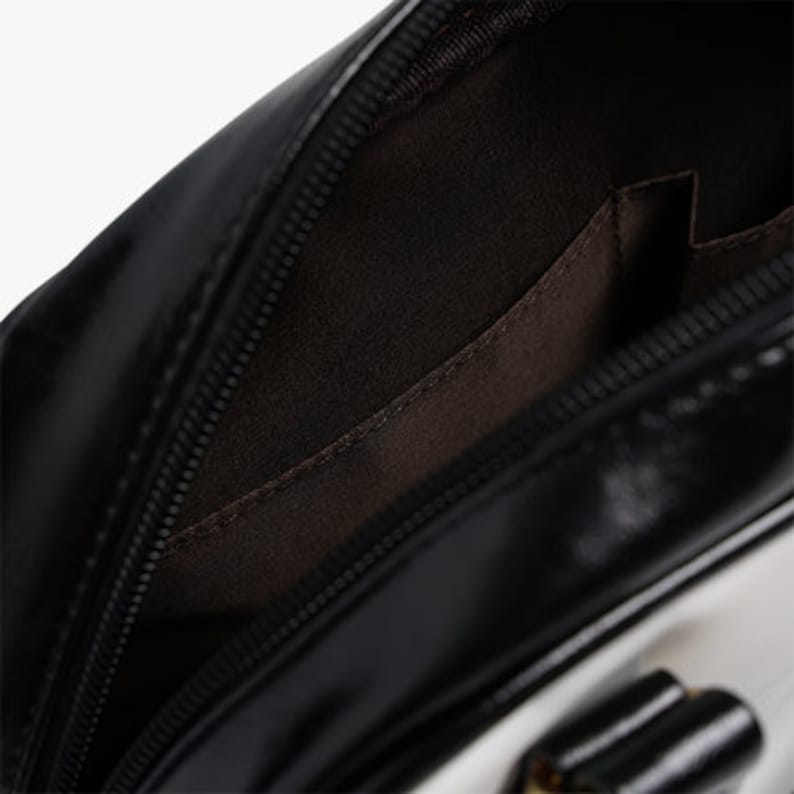 May include: Black and white leather handbag with a zipper closure and a small interior pocket. The bag has a smooth, shiny finish.