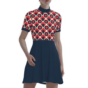 May include: A short-sleeved dress featuring a retro geometric pattern in red, black, and cream on the bodice. The dress has a high neckline and a solid navy blue skirt. The dress is knee-length and has a fitted bodice and a flared skirt.