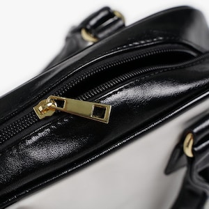 May include: Close-up of a black leather handbag with a gold zipper pull. The bag has a white lining and a gold handle.