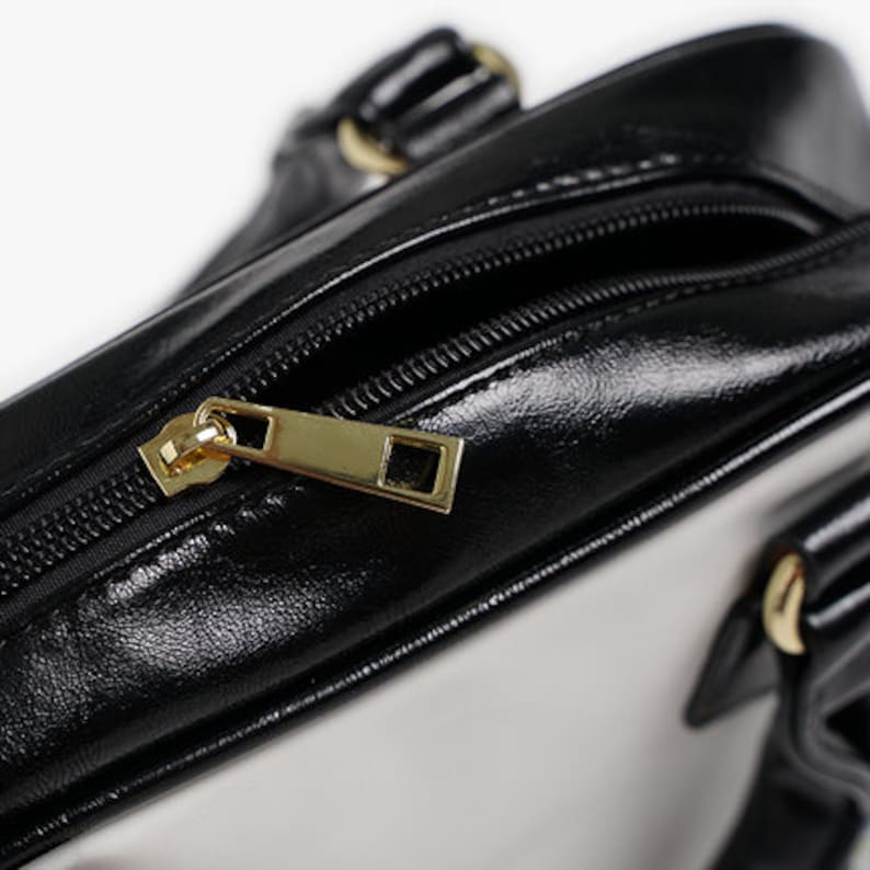 May include: Close-up of a black leather handbag with a gold zipper pull. The bag has a white lining and a gold handle.