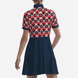 May include: A navy blue dress with a high collar and short sleeves. The bodice features a retro geometric pattern in red, cream, and navy blue circles. The dress has a flared skirt.