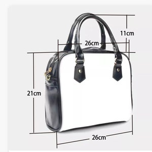 May include: White satchel handbag with black trim and a black handle. The bag measures 26 inches wide, 21 inches tall, and 11 inches deep.