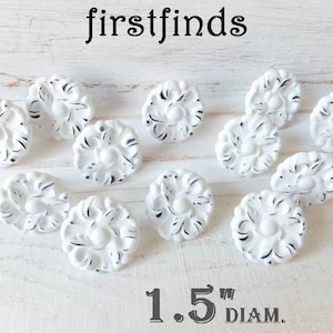 May include: A collection of 12 white ceramic drawer pulls with a decorative floral design. Each pull measures 1.5 inches in diameter.